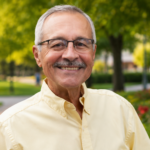 "Jesus Lechuga smiling outdoors in a professionally edited portrait, wearing glasses and a light-colored shirt, standing in a scenic park with lush greenery, colorful flowers, and a softly blurred background."